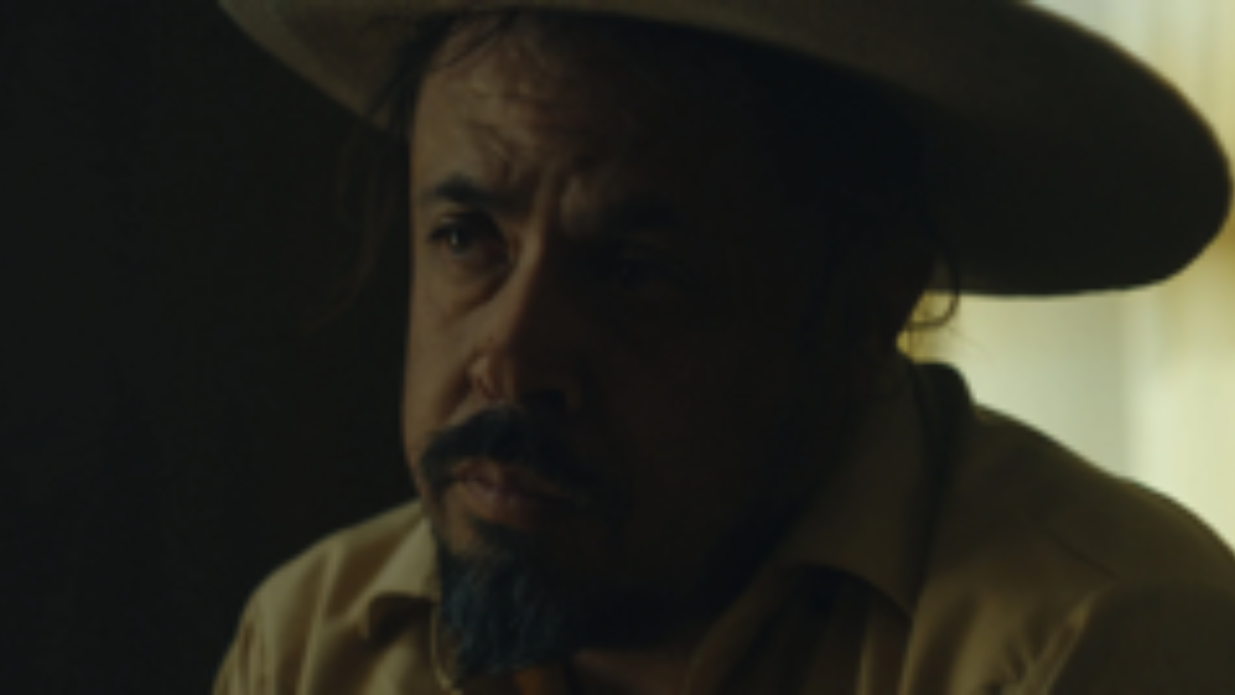 A man in a wide-brimmed hat sits in soft window light, captured with cinematic intimacy.