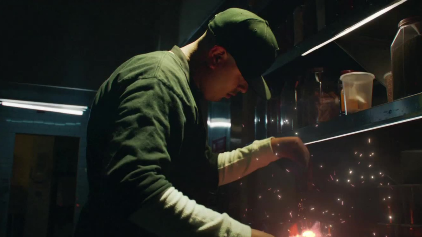 A chef works intently under dramatic lighting, sparks flying as culinary creativity meets industrial grit in a behind-the-scenes moment.