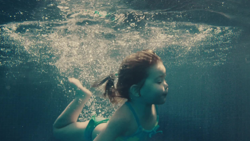 A young girl swims freely underwater, capturing a poetic sense of innocence and resilience in a world transformed.
