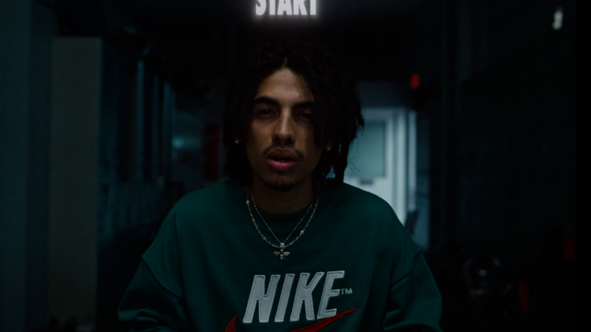 A young man in a Nike sweatshirt faces the camera under a glowing “START” sign.