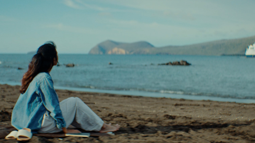 A woman sits on a beach gazing at distant islands across the sea.
