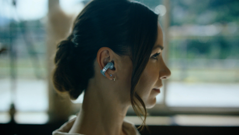 A close profile of a woman wearing modern earbuds, framed by soft indoor light.