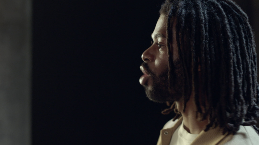 A dramatic profile shot of a man with locs, lit with soft edge lighting against a black background, creating an intimate and cinematic portrait.