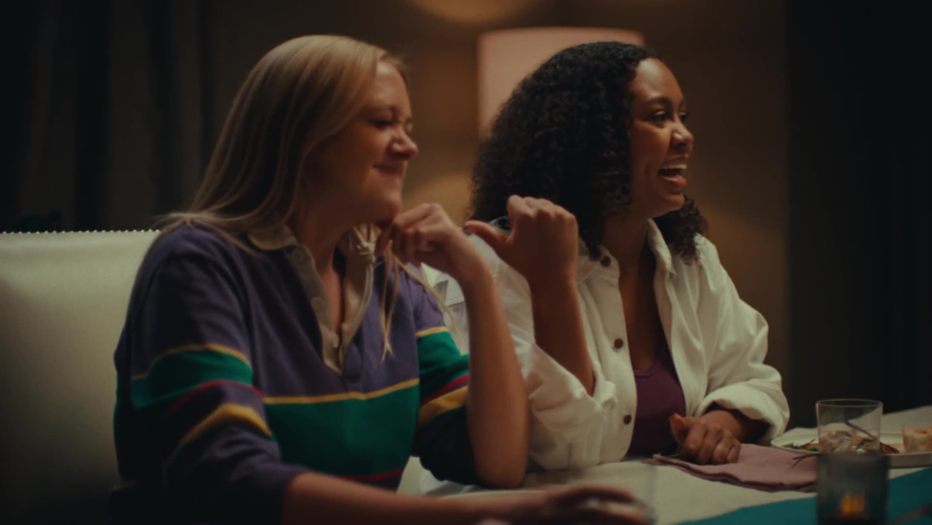 Two women laugh mid-conversation at a warmly lit dinner table, their relaxed gestures and genuine expressions conveying connection and camaraderie.