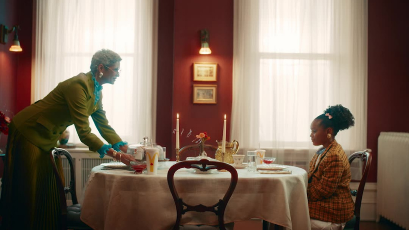 A stylized dining scene with a bold color palette and symmetrical composition that evokes theatricality and charm while emphasizing generational storytelling.