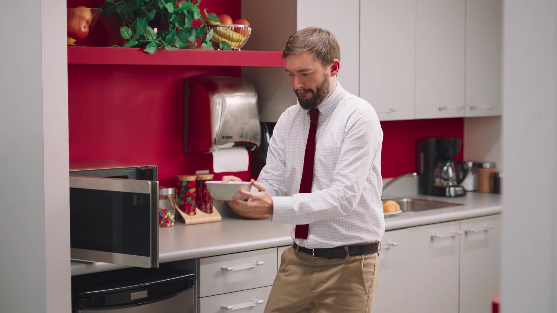 A man in a shirt and tie preps a quick meal in a bright red and white kitchen.