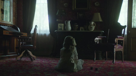 A small dog sits alone in a dim, ornate vintage living room looking toward the window