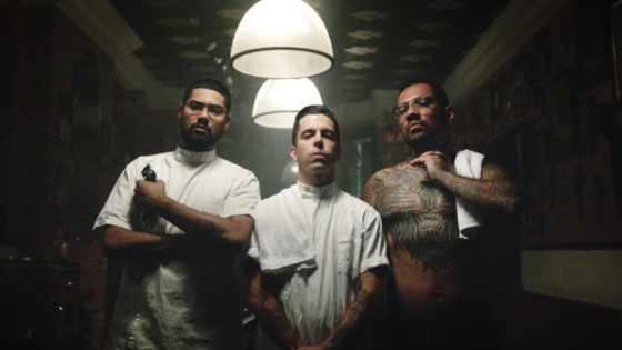 Three men pose together under a single overhead light in a moody, vintage-styled room