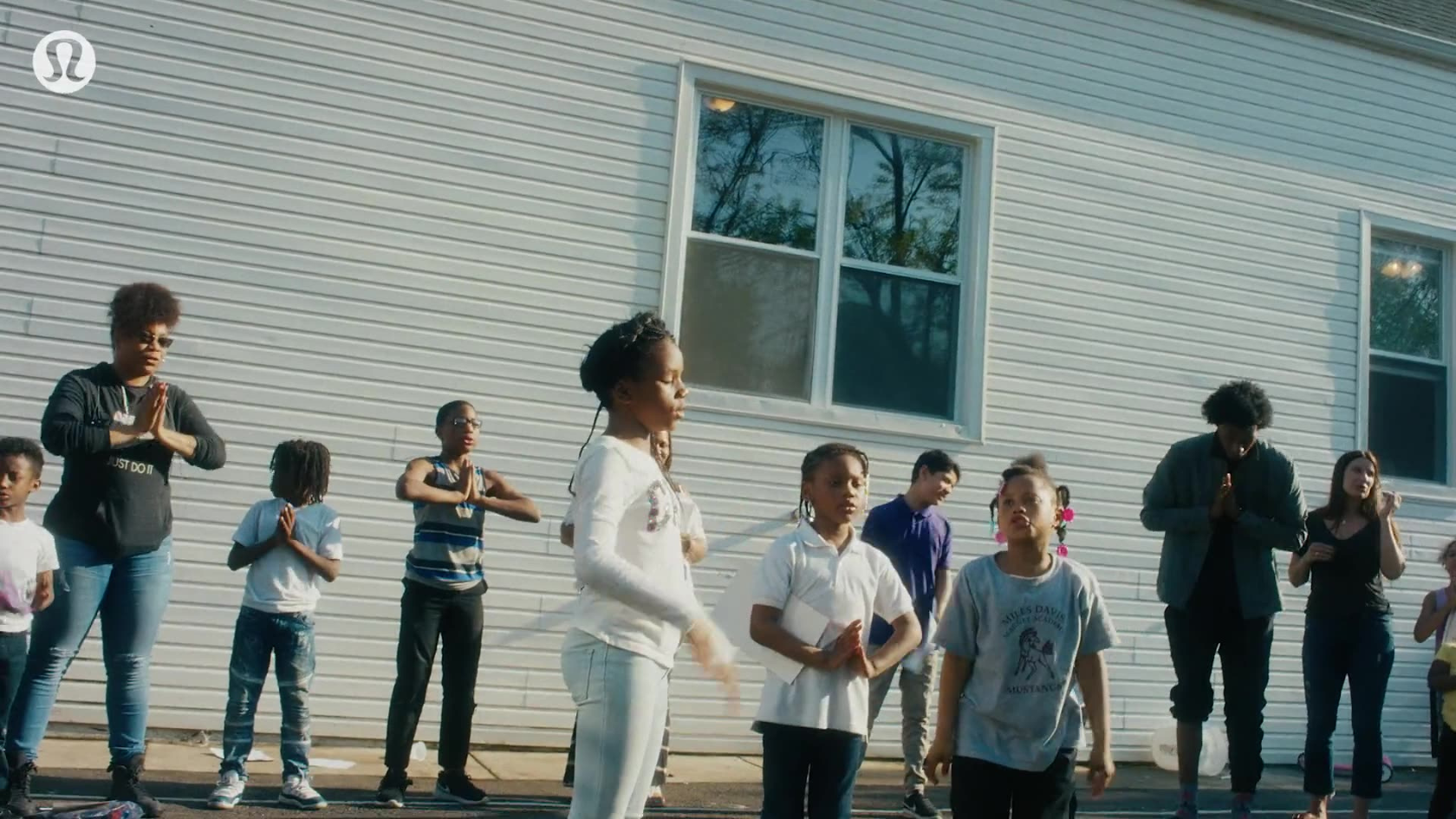 Community yoga class assembles outdoors in matching attire, centered on an instructor leading mindful practice against a residential backdrop.