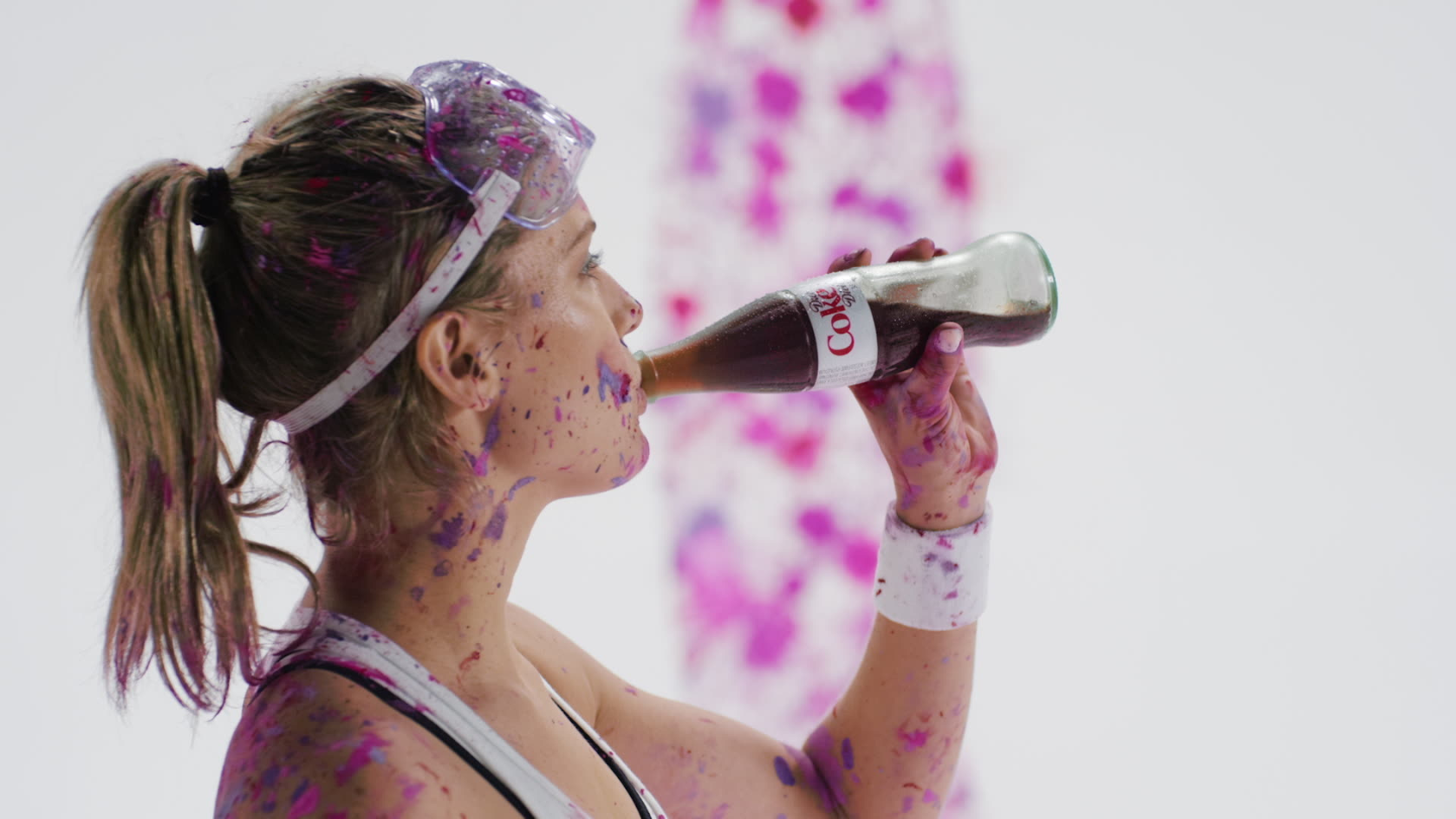 High-energy athletic portrait of a runner mid-action, covered in vibrant purple color powder while hydrating with a branded beverage.