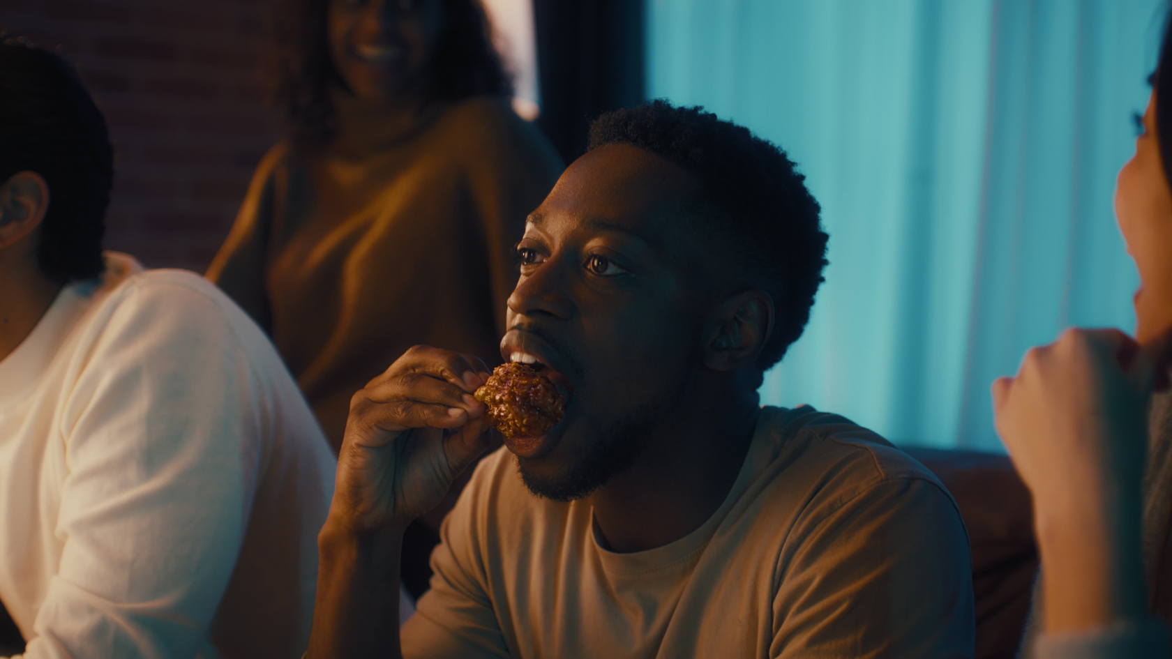 Intimate moment of connection as friends share food and laughter, lit with moody teal and warm amber tones.