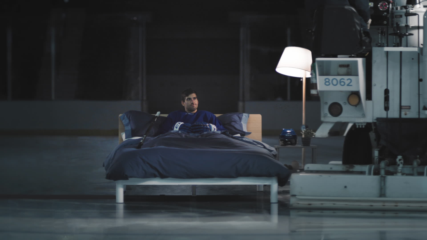 Surreal wide shot of an insomniac alone in a vast industrial space, emphasizing isolation through dramatic scale and cool lighting.