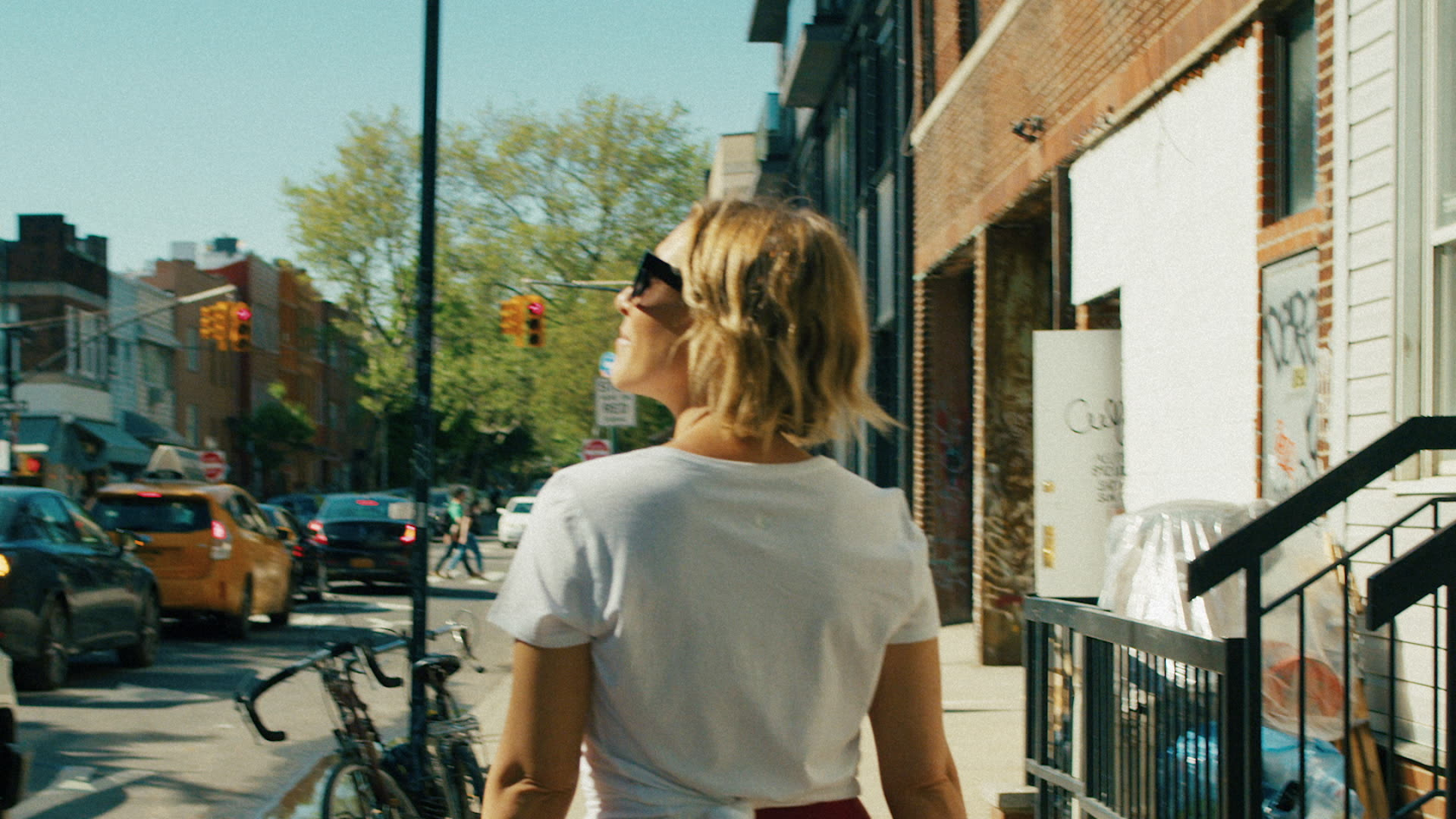 Handheld street POV follows a woman walking through a sunny urban neighborhood, capturing authentic city life in motion.