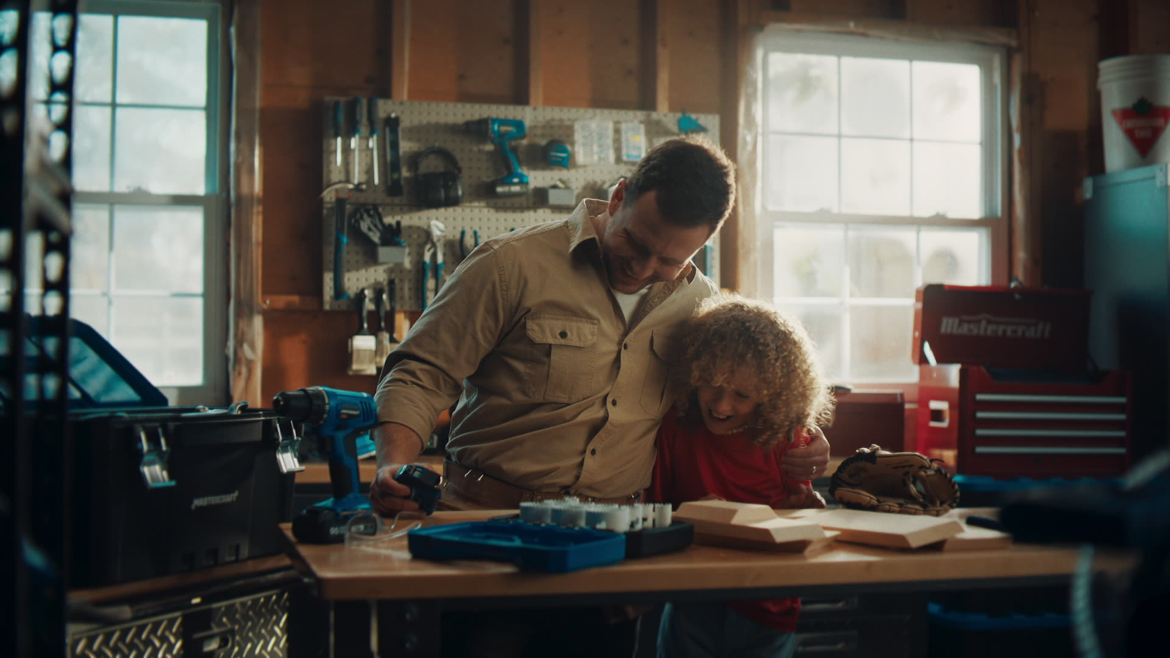 Father and son share a quiet workshop moment, bathed in natural window light as they collaborate on a woodworking project.