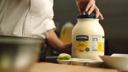 Photo of a chef hand opening a large container of hellmans mayo. Limes and  bowl are in the background.