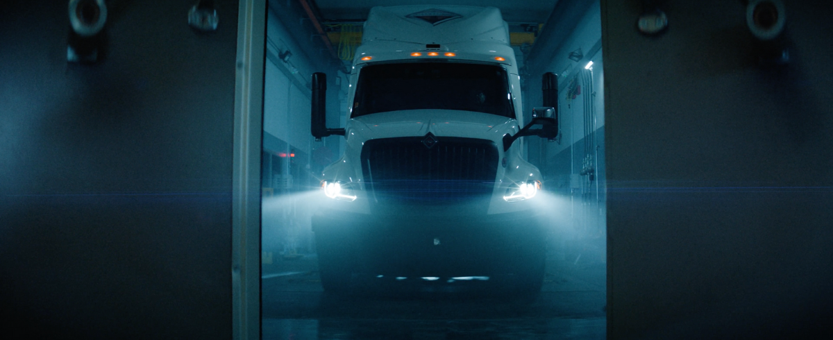 Large white truck with headlights on inside a garage.