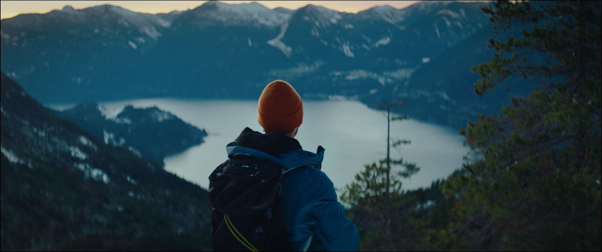 A man gazing at a picturesque snowy lake surrounded by snow-covered mountains.