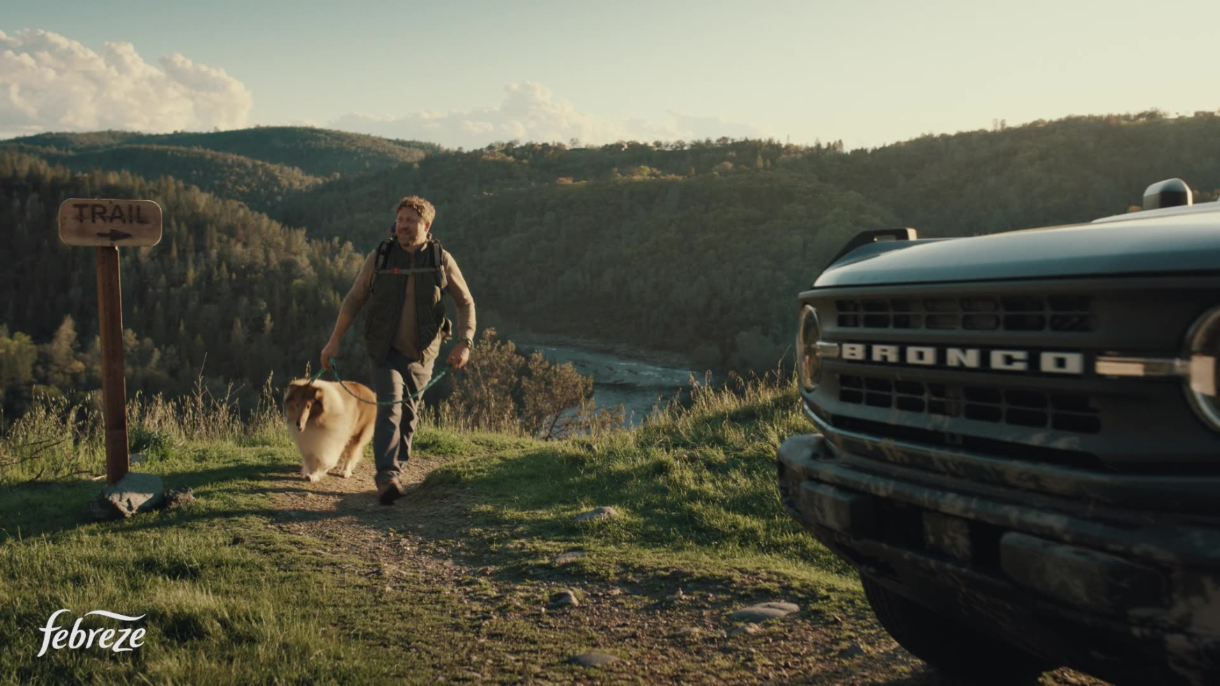 A man walks toward a vintage school bus parked on a scenic forest overlook at golden hour.