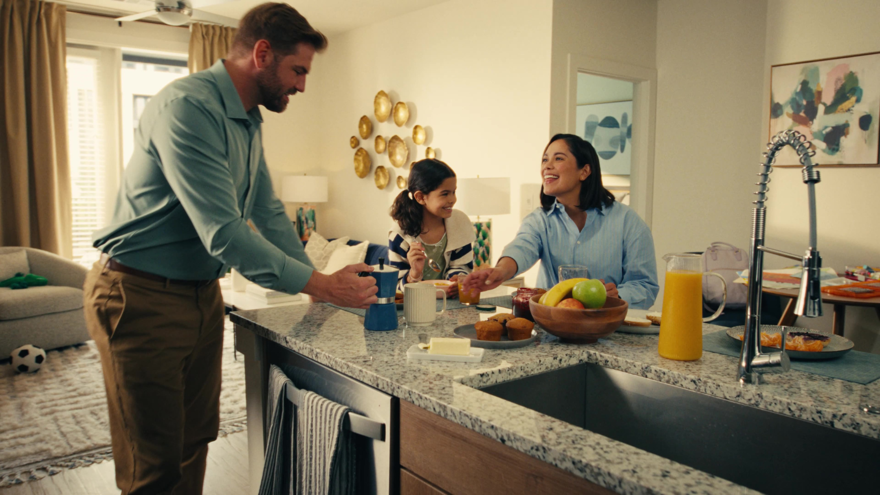A family gathers around the kitchen counter sharing a meal together in a warmly lit home.