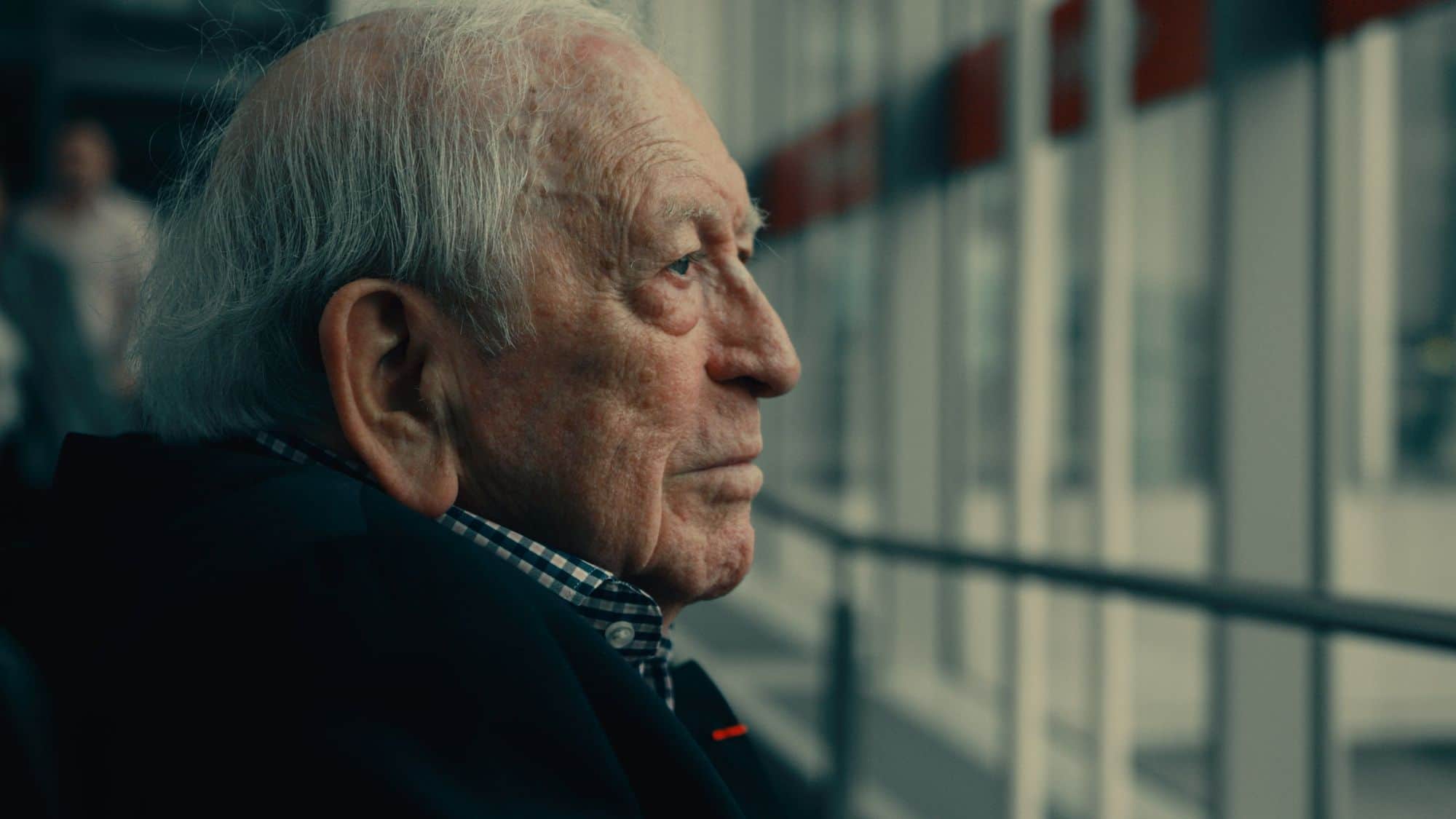 A photo of an old man veteran sitting in front of the window at the airport looking out to his airplane. 