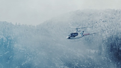 helicopter flying over snowy trees and hills. 