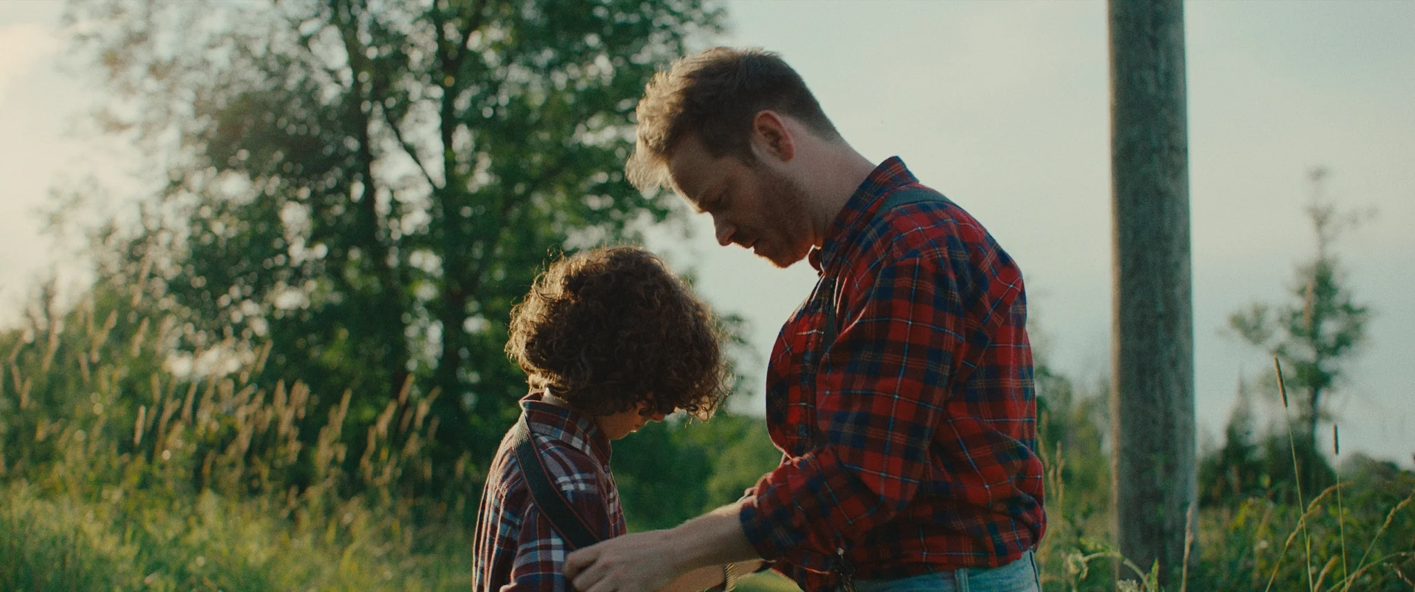 Man kneeling in a field next to a young boy holding his arms