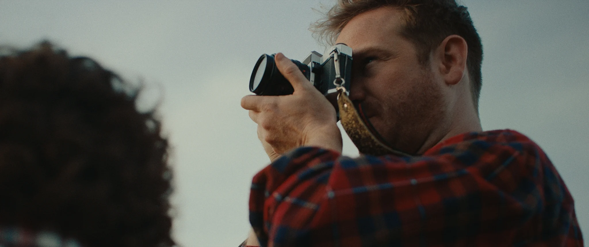 Photo of a man taking a picture with a camera, boy with curly hair in corner of image