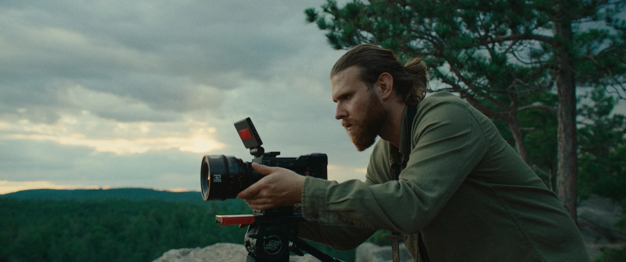 man crouching on mountain top with camera in hand