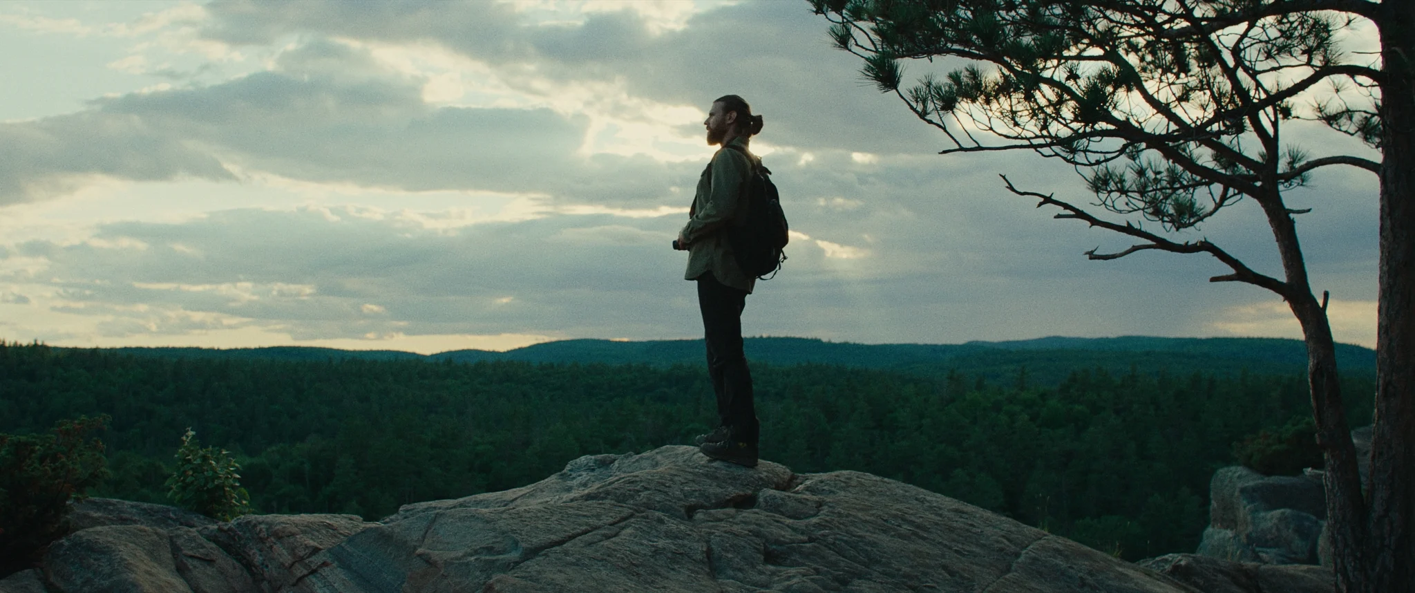 Man standing on a mountain top overlooking the trees holding a camera in hand